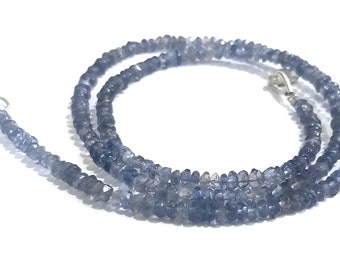 May include: A necklace composed of small, faceted, blue-gray gemstones. The beads are strung together, forming a multi-strand design. The necklace has a silver-colored clasp. The gemstones have a slightly irregular shape, adding to their natural appearance.