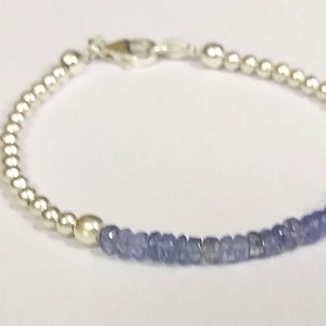 May include: A silver bracelet with a row of small, light blue gemstone beads.