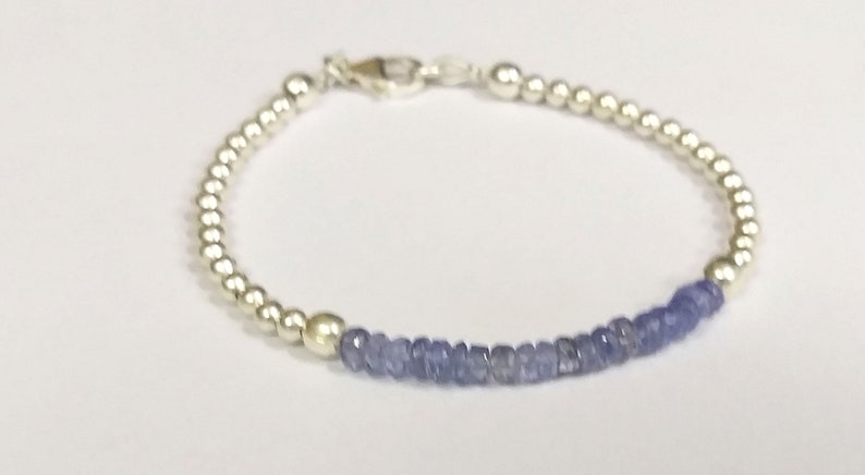 May include: A silver bracelet with a row of small, light blue gemstone beads.