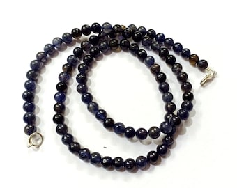 May include: A dark blue gemstone necklace with silver clasps. The necklace is made of round beads and is approximately 18 inches long.