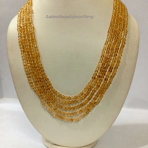 May include: A multi-strand necklace made of small, round, translucent amber beads. The necklace is displayed on a white mannequin bust.