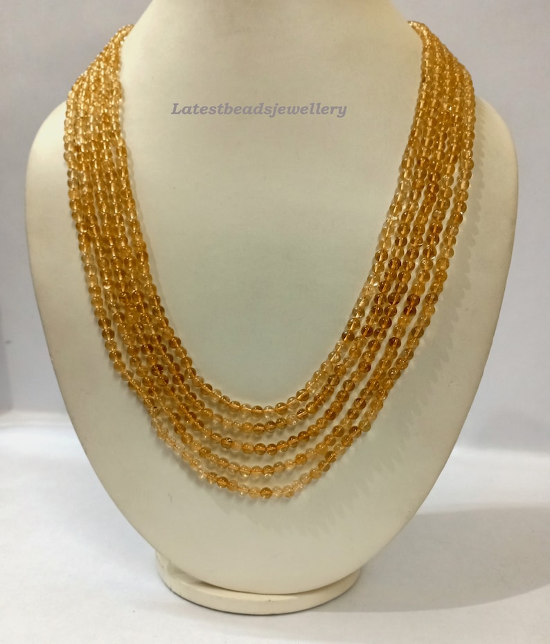 May include: A multi-strand necklace made of small, round, translucent amber beads. The necklace is displayed on a white mannequin bust.