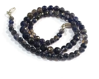 May include: A necklace made of dark blue and gray gemstone beads. The beads are faceted and have a slightly irregular shape. The necklace is strung on a silver chain and has a silver clasp.