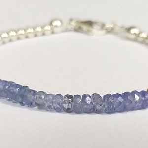 May include: A silver bracelet with a row of light blue gemstone beads. The bracelet has a silver clasp.