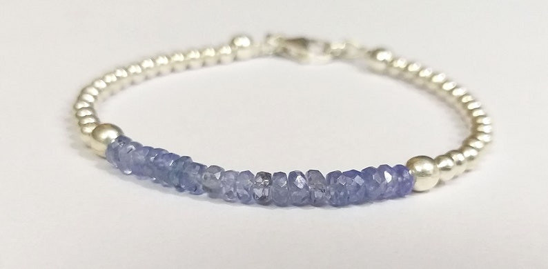 May include: A silver bracelet with a row of light blue gemstone beads. The bracelet has a silver clasp.