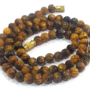 May include: A brown and gold tiger's eye beaded necklace with a carved flower design on each bead. The necklace has a gold clasp.