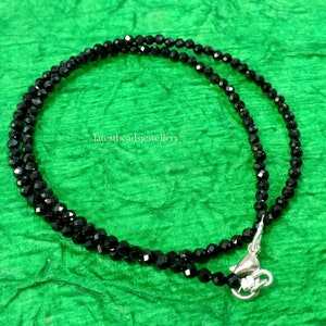 Op de afbeelding: Een zwarte kralenketting met een zilveren sluiting. De ketting is gemaakt van kleine, gefacetteerde kralen en is ongeveer 45 cm lang.