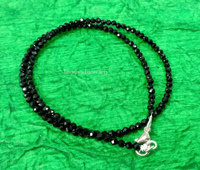 Op de afbeelding: Een zwarte kralenketting met een zilveren sluiting. De ketting is gemaakt van kleine, gefacetteerde kralen en is ongeveer 45 cm lang.