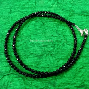 Op de afbeelding: Een zwarte kralenketting met een zilveren sluiting. De ketting is gemaakt van kleine, gefacetteerde kralen en is ongeveer 45 cm lang.