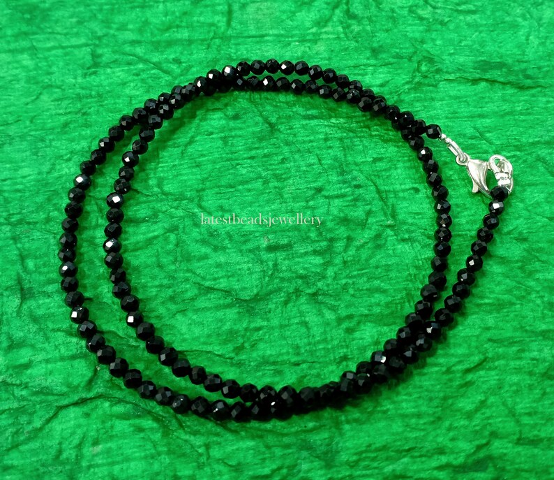 Op de afbeelding: Een zwarte kralenketting met een zilveren sluiting. De ketting is gemaakt van kleine, gefacetteerde kralen en is ongeveer 45 cm lang.