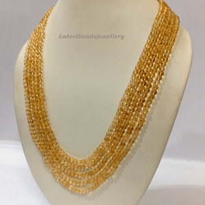 May include: A multi-strand necklace made of light amber beads. The necklace is displayed on a white mannequin bust. The text "Latestbeadsjewellery" is visible on the bust.