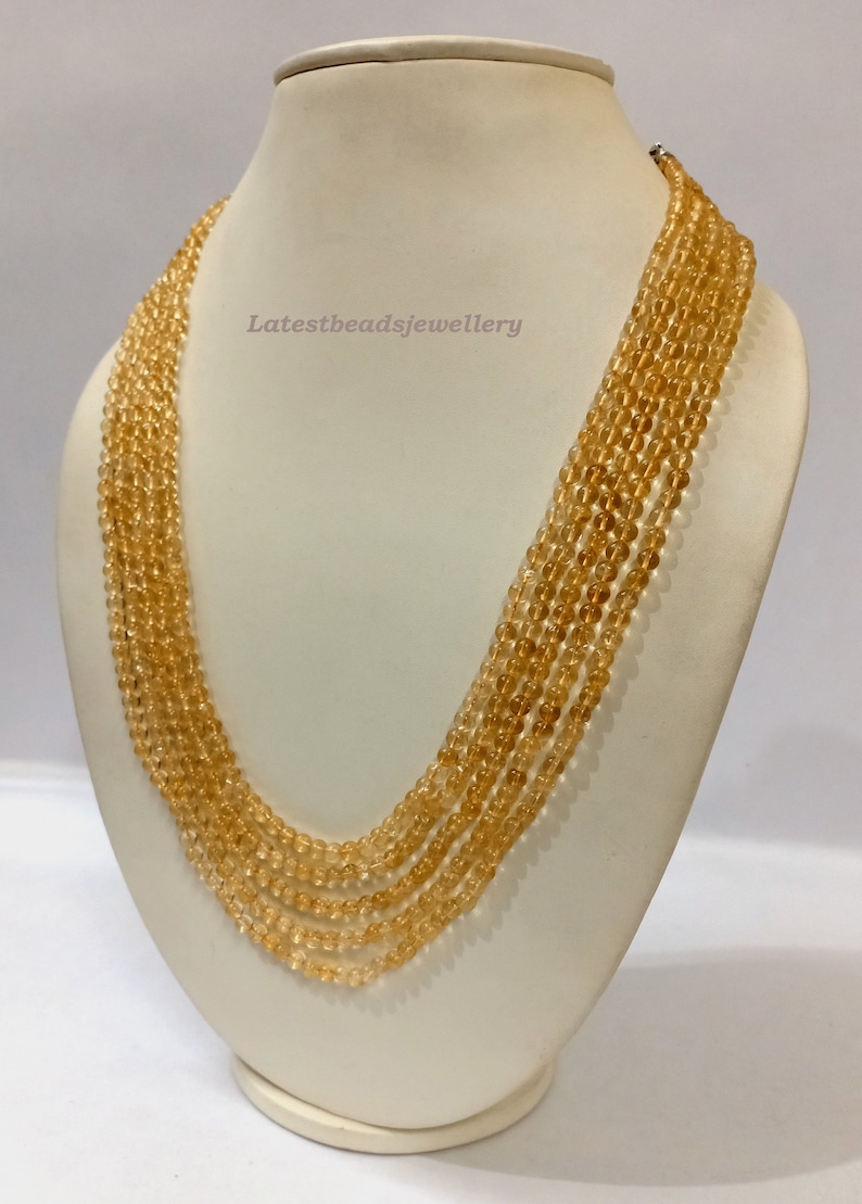 May include: A multi-strand necklace made of light amber beads. The necklace is displayed on a white mannequin bust. The text "Latestbeadsjewellery" is visible on the bust.