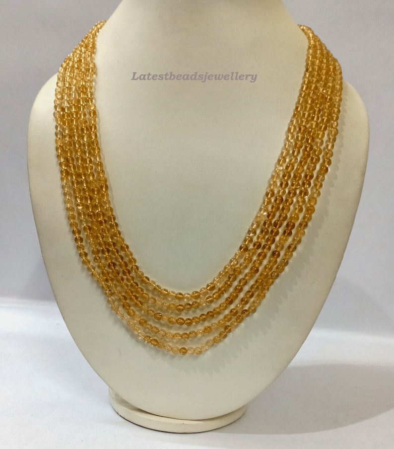 May include: A multi-strand necklace made of small, round, golden-brown beads. The necklace is displayed on a white mannequin bust. The text "Latestbeadsjewellery" is visible on the bust.