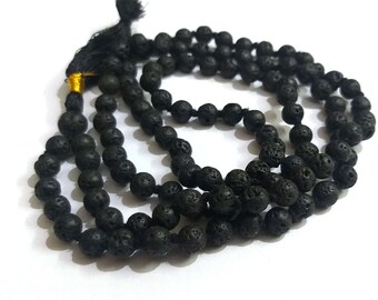 Puede incluir: Collar de cuentas de piedra de lava negra con borla. Las cuentas redondas tienen una textura porosa. El collar está ensartado en un cordón negro y tiene una borla negra con detalles dorados.