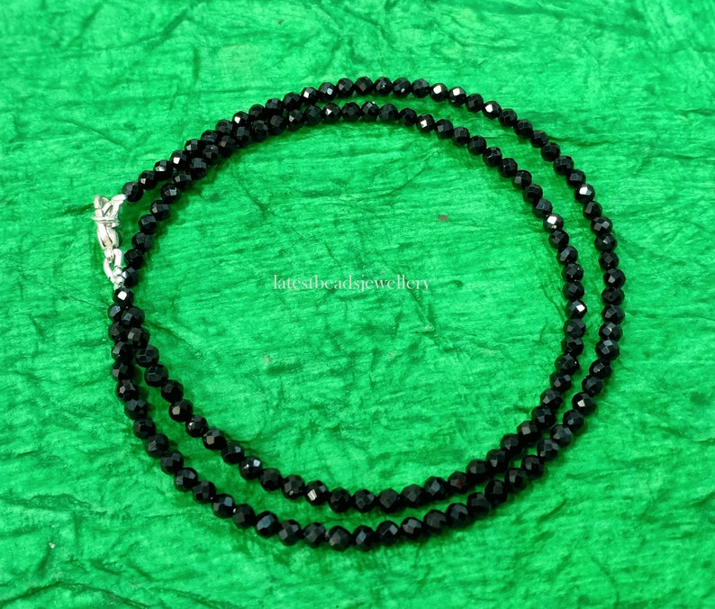 Op de afbeelding: Een zwarte kralenketting met een zilveren sluiting. De ketting is gemaakt van kleine, gefacetteerde kralen en is ongeveer 45 cm lang.