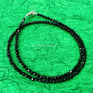 Op de afbeelding: Een dubbele rij zwarte kralenketting met een zilveren sluiting. De ketting ligt op een groene achtergrond.