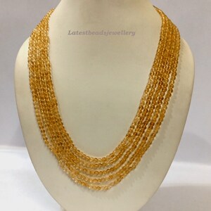 May include: A multi-strand necklace made of small, round, golden-brown beads. The necklace is displayed on a white mannequin bust. The text "Latestbeadsjewellery" is visible on the bust.
