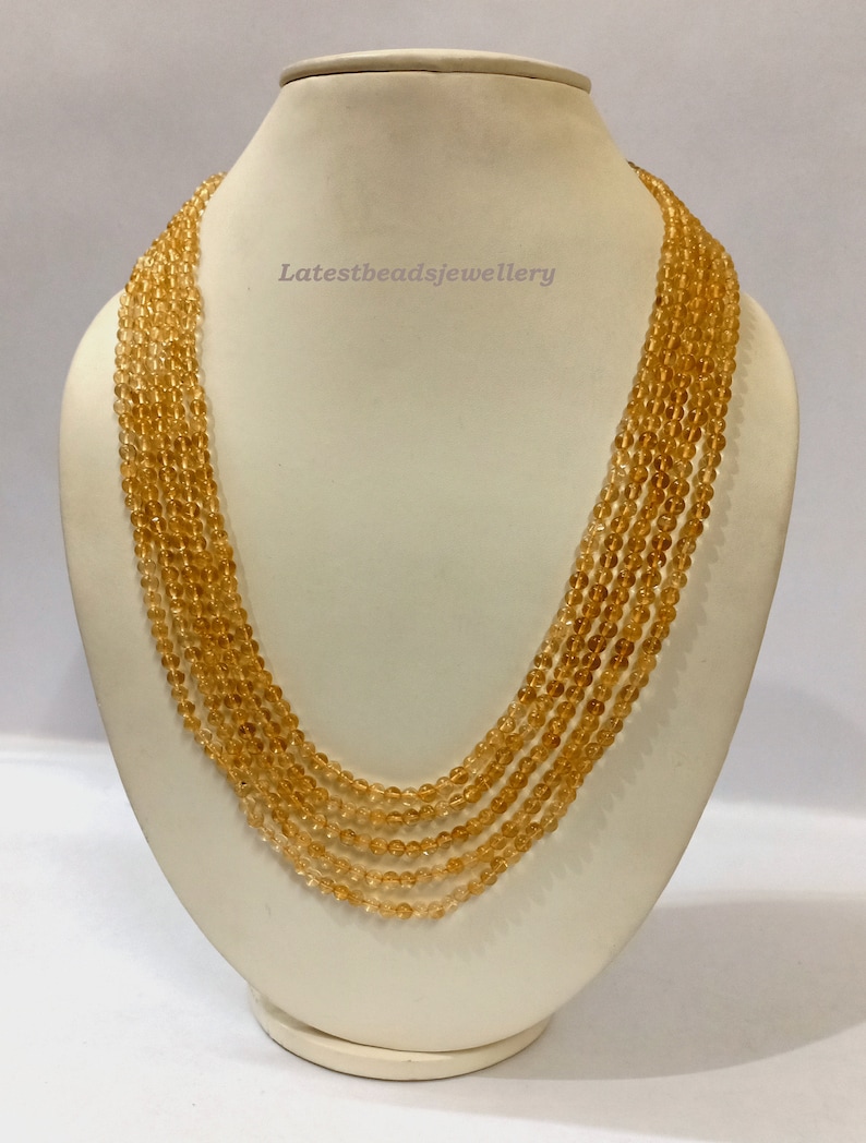 May include: A multi-strand necklace made of small, round, golden-brown beads. The necklace is displayed on a white mannequin bust. The text "Latestbeadsjewellery" is visible on the bust.