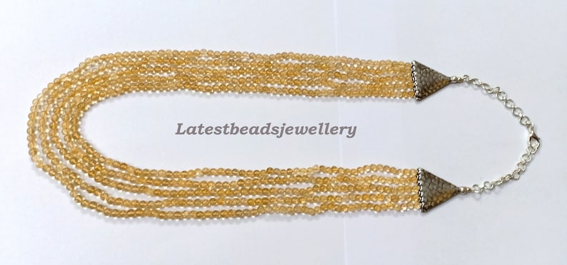 May include: A multi-strand necklace made of light brown beads with silver end caps and a silver chain closure. The necklace is on a white background. Latestbeadsjewellery is printed in black text on the background.