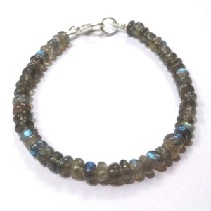 May include: A silver beaded bracelet with a silver clasp. The beads are a dark grey color with iridescent blue and green flashes.