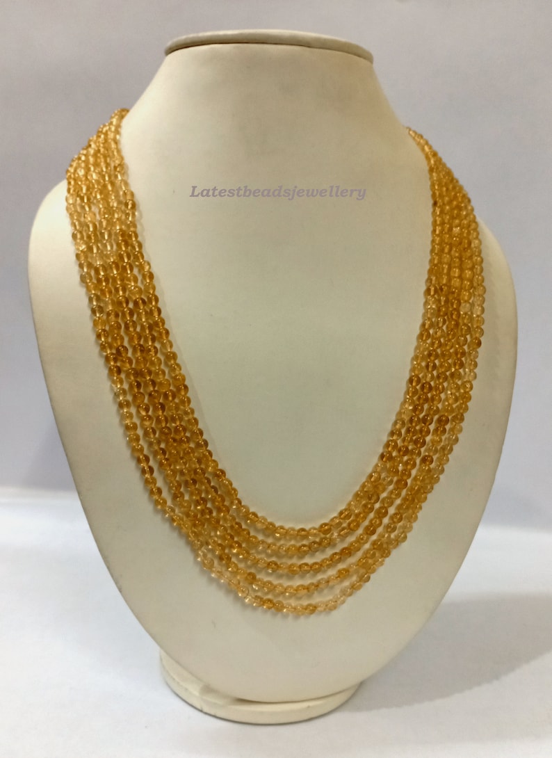 May include: A multi-strand necklace made of round, translucent, amber-colored beads. The necklace is displayed on a white mannequin bust.
