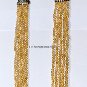 May include: A multi-strand necklace made of light brown beads with silver triangle end caps. The necklace is on a white background.