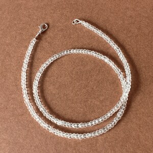 Könnte beinhalten: Eine klare Kristallperlenkette mit einem silbernen Verschluss. Die Kette besteht aus kleinen, facettierten Perlen und ist etwa 45 cm lang.