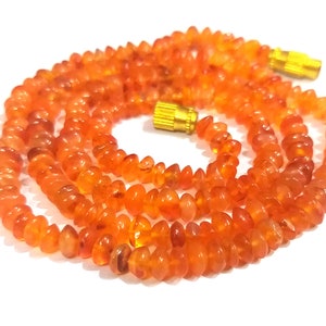 May include: A long strand of orange carnelian beads with gold-toned clasps. The beads are faceted and have a smooth, polished finish.