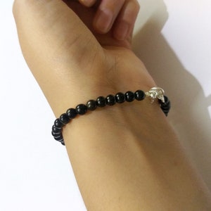 May include: A black beaded bracelet with a silver clasp. The bracelet is worn on a person's wrist.
