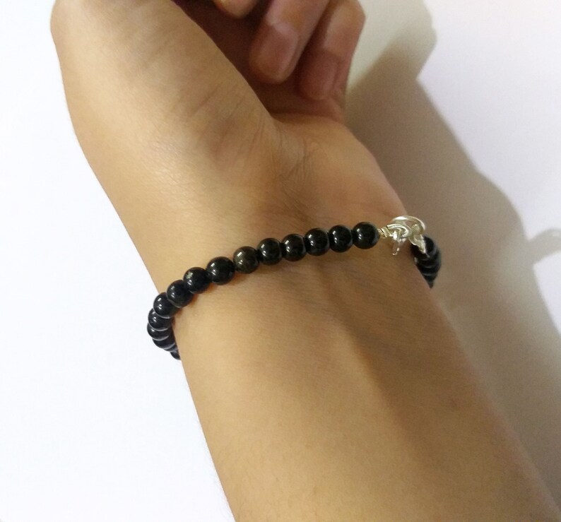 May include: A black beaded bracelet with a silver clasp. The bracelet is worn on a person's wrist.