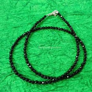 Op de afbeelding: Een zwarte kralenketting met een zilveren sluiting. De ketting is gemaakt van kleine, ronde kralen en is ongeveer 45 centimeter lang.