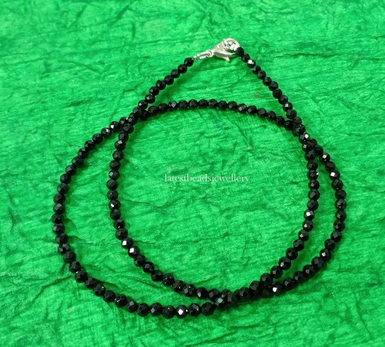 Op de afbeelding: Een zwarte kralenketting met een zilveren sluiting. De ketting is gemaakt van kleine, ronde kralen en is ongeveer 45 centimeter lang.