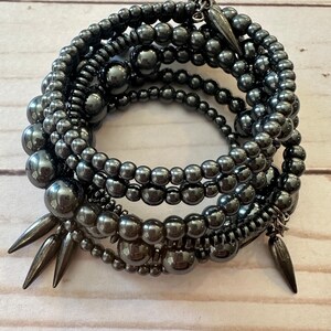 May include: A multi-strand bracelet made of black beads of varying sizes. The bracelet features several metal spikes and a decorative charm.