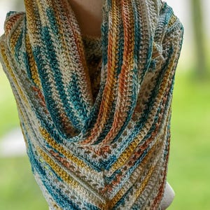 May include: A handmade crochet shawl in a triangular shape, displayed on a mannequin. The shawl features a mix of colors including teal, yellow, orange, and white. The open weave design adds to its visual appeal. The shawl is a cozy accessory.