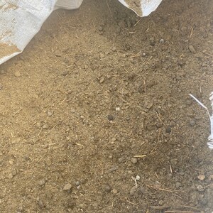 May include: A close-up of a white bag filled with brown soil and small twigs.