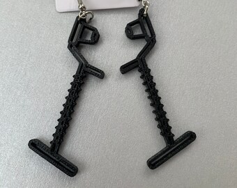 May include: A pair of black earrings shaped like a stylized figure with a textured surface. The earrings are attached to silver hooks.
