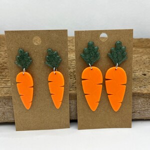 May include: A pair of carrot-shaped earrings with green glitter leaves. The earrings are made of orange and green polymer clay and are attached to silver ear wires.