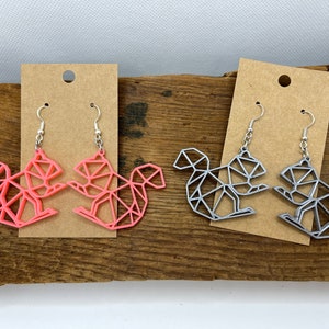 May include: Two pairs of geometric squirrel earrings. One pair is pink and the other is silver.