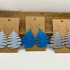 May include: Three pairs of dangle earrings with a leaf design. The earrings are made of a textured material and come in blue, gray, and white.