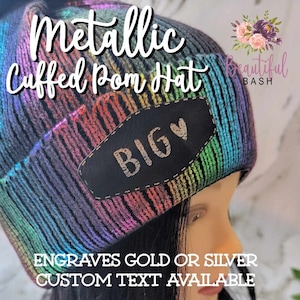 May include: Metallic rainbow knit cuffed beanie with a black faux fur pom pom and a black leather patch that says "BIG" in gold lettering. The hat is available with custom text engraved in gold or silver.