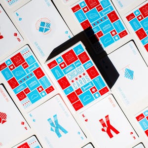 May include: A deck of "Chicago Cards" playing cards, featuring red and blue designs on a white background. The cards display various Chicago-themed icons and the text "CHICAGO CARDS". The cards are arranged on a white surface.