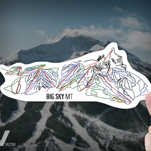 May include: A white sticker with a black outline of a ski resort map. The map shows the different runs and lifts at Big Sky Mt. The sticker is held in a hand against a background of a snowy mountain.