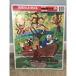 Puede incluir: Un rompecabezas vintage de Donald Duck con marco-bandeja que presenta a Donald Duck y otros personajes en un bote en un entorno de selva. El rompecabezas está hecho por Golden y es para niños de 3 a 7 años. El rompecabezas tiene una imagen en la parte posterior.
