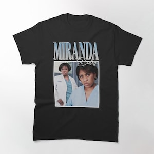 May include: Black t-shirt with a vintage-style graphic of Miranda Bailey from the TV show Grey's Anatomy. The graphic features a photo of Miranda Bailey in her scrubs with the text "Miranda Bailey" above her.
