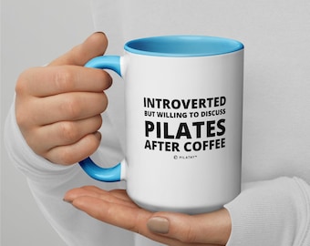 May include: White ceramic mug with a light blue rim and handle. The mug has black text that reads "Introverted but willing to discuss Pilates after coffee" with a small copyright symbol and the word "Pilatay" below the text.