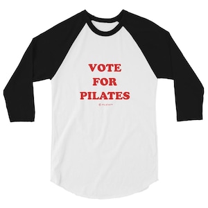 Könnte beinhalten: Ein weißes und schwarzes Baseball-T-Shirt mit rotem Text, der "VOTE FOR PILATES" lautet, mit einem kleinen Copyright-Symbol und "PILATATM" darunter.