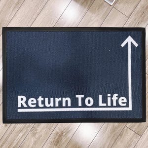 Op de afbeelding: Een blauwe deurmat met een zwarte rand en witte tekst die "Return To Life" zegt met een pijl die omhoog wijst.