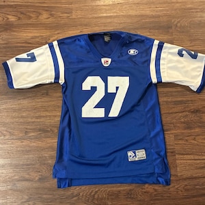 Könnte beinhalten: Ein blaues Football-Trikot mit weißen Ärmeln und der Nummer 27 in Weiß. Das Trikot hat einen V-Ausschnitt und ein Starter-Logo. Die Ärmel haben die Nummern 1 und 2 in Weiß.
