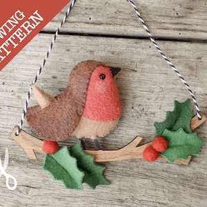 May include: A felt Christmas ornament sewing pattern featuring a red-breasted robin perched on a brown branch with green holly leaves and red berries. The pattern includes instructions for sewing the robin, branch, and holly.