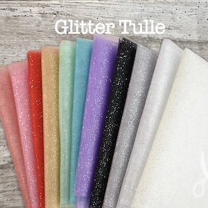 May include: A collection of ten folded sheets of glitter tulle fabric in various colours including pink, red, gold, mint, blue, purple, black, silver, and white, arranged in a fan shape with the text Glitter Tulle printed at the top.